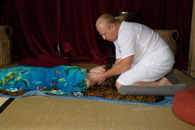 Sergio kneeling at the head of a client who lies on her back, cradling her head and neck in his hands